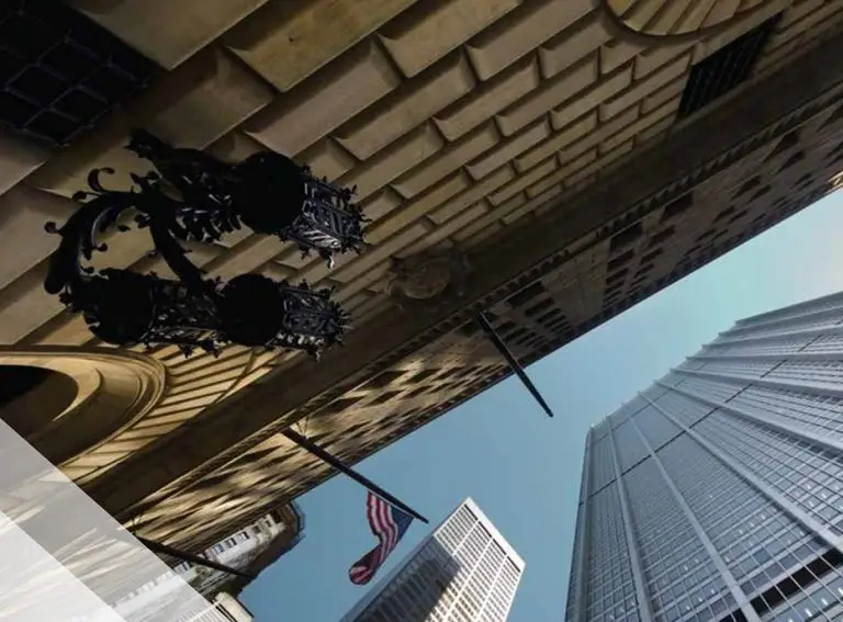A dramatic upward view of tall city buildings with ornate black street lamps, an American flag, and a clear blue sky—striking angles and shadows evoke the robust security standards of the FedRAMP Marketplace.